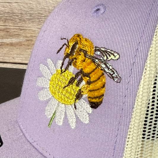Cap with embroidered bee and flower design on a wooden surface