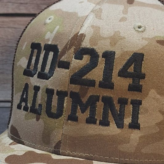 Camouflage cap with 'DD-214 ALUMNI' text on a wooden surface