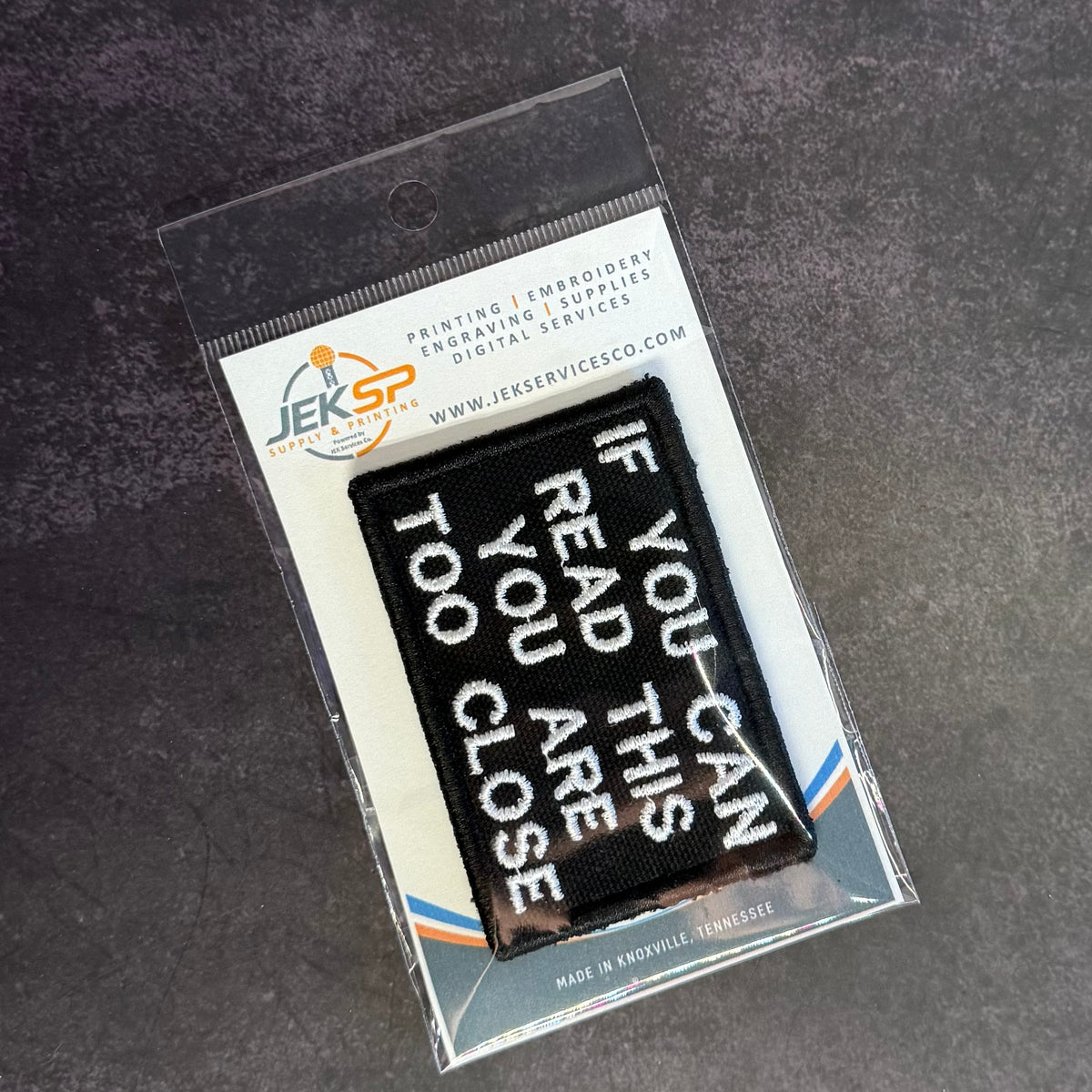 If You Can Read This You Are Too Close embroidered morale patch: rectangular embroidered patch with white text reading 'IF YOU CAN READ THIS YOU ARE TOO CLOSE' inside a clear plastic retail sleeve on a dark textured background.