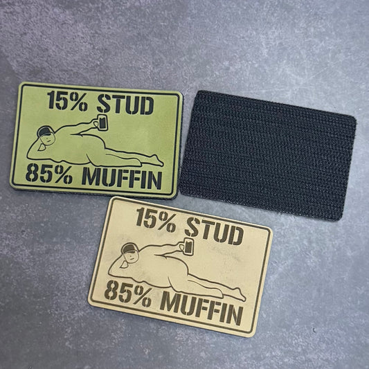 Two rectangular embroidered patches with the text '15% STUD 85% MUFFIN' and a simple figure graphic, shown on a gray textured background. One patch is olive green and the other is tan, both with black embroidered outlines.