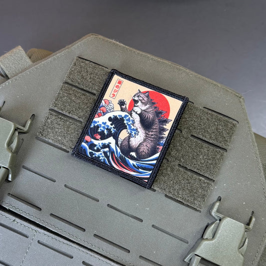 A rectangular tactical patch featuring a Japanese ukiyo-e style cat under a red sun and blue waves, mounted on olive drab MOLLE webbing of a tactical vest.