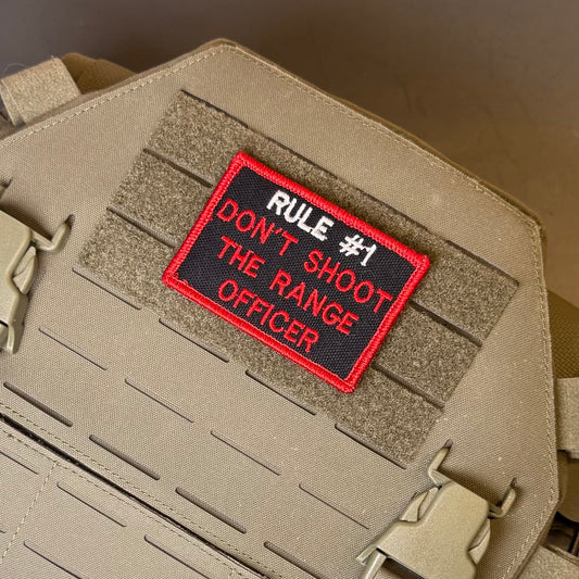 Rule #1 Don't Shoot The Range Officer embroidered morale patch: embroidered tactical patch with red border and black background reading 'RULE #1 DON'T SHOOT THE RANGE OFFICER' in white and red text, shown attached to tan webbing.