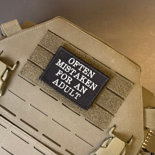 Often Mistaken For An Adult embroidered morale patch: tactical bag in coyote tan with a black rectangular patch featuring the white text 'OFTEN MISTAKEN FOR AN ADULT' on a tan background.
