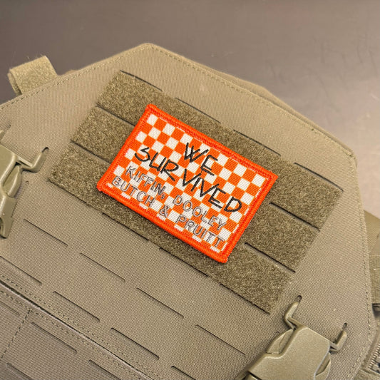 We Survived, Tennessee Football embroidered morale patch: tactical patch with an orange border and a white-and-orange checkered top, reading 'WE SURVIVED KAREN DOOLEY' in black script, shown attached to tan webbing on a matching.