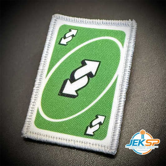 A rectangular embroidered patch featuring a green background with a white oval, double arrows, and two small white arrows, shown on a dark textured surface. A JEKSP watermark is visible in the bottom right corner.