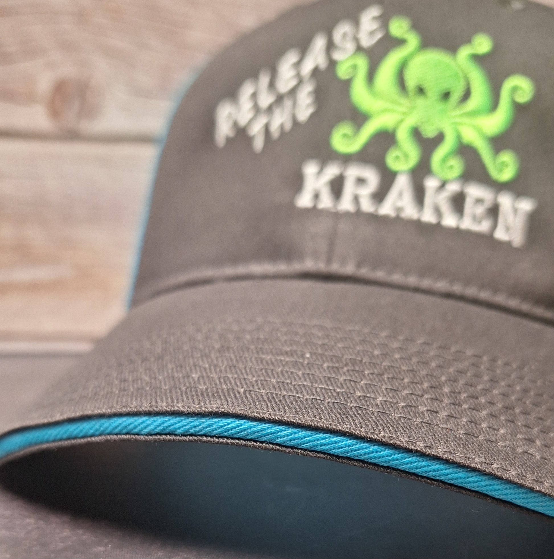 Gray cap with green octopus design and text 'Release the Kraken' on a wooden surface