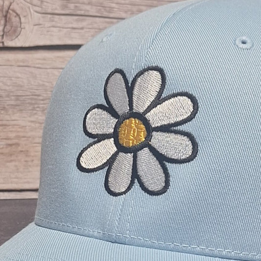 Light blue cap with a embroidered daisy flower design on a wooden surface