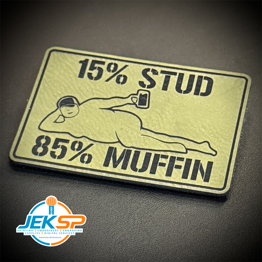 A rectangular novelty patch with rounded corners featuring a black graphic and text on a metallic gold background. The patch reads '15% STUD 85% MUFFIN' with a line drawing of a person lying down holding a phone.