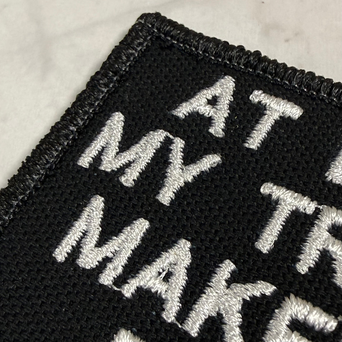 Close-up of a black embroidered patch with white lettering on a light marble surface.