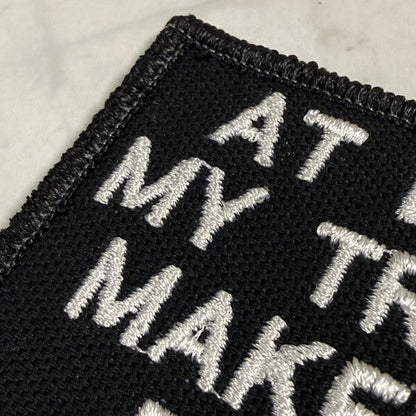 Close-up of a black embroidered patch with white lettering on a light marble surface.