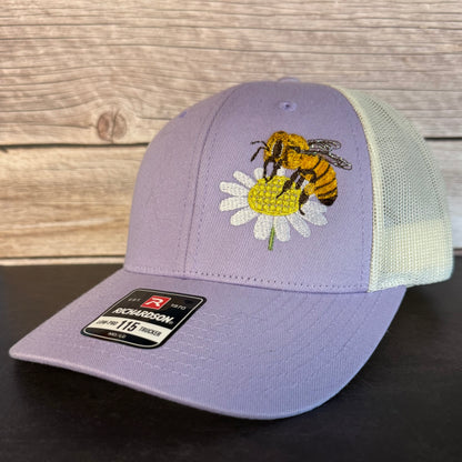 Purple cap with bee and flower design on a wooden surface