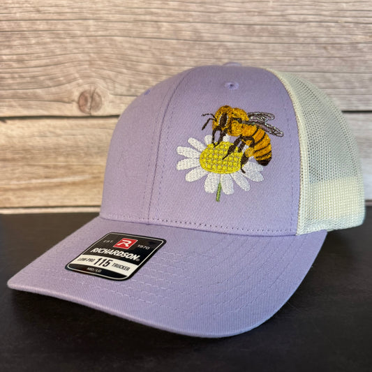 Purple cap with bee and flower design on a wooden surface