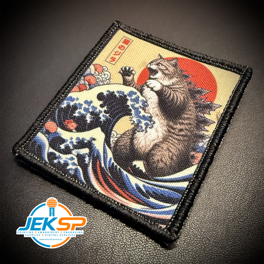 A square embroidered tactical patch featuring a Japanese-style cat wave scene with a roaring cat, blue waves, a red sun, and a beige background, shown on a dark textured surface. A JEKSP brand watermark is visible in the bottom-left corner.