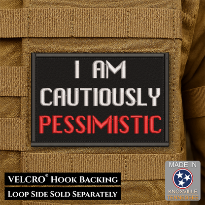 A rectangular black Velcro patch with the text 'I AM CAUTIOUSLY PESSIMISTIC' in white and red lettering, shown attached to tan tactical gear. Text at the bottom notes VELCRO® Hook BACKING and LOOP SIDE SOLD SEPARATELY, with a Made in Knoxville Tennessee badge in the lower right.