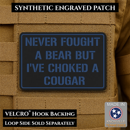 I’ve Choked A Cougar laser-engraved synthetic morale patch: a rectangular synthetic engraved patch with a dark charcoal background and blue border and lettering, shown attached to tan tactical vest loops. Text overlays read.