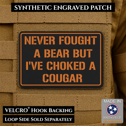 I’ve Choked A Cougar laser-engraved synthetic morale patch: a rectangular black synthetic patch with orange border and orange text reading “NEVER FOUGHT A BEAR BUT I’VE CHOKED A COUGAR,” shown attached to tan tactical fabric. Text.