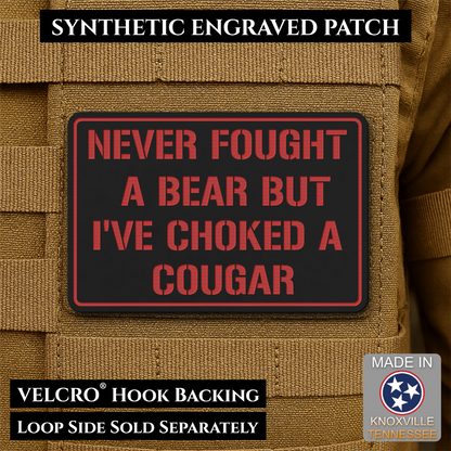 I’ve Choked A Cougar laser-engraved synthetic morale patch: a rectangular black synthetic patch with red border and red text reading “NEVER FOUGHT A BEAR BUT I’VE CHOKED A COUGAR,” shown attached to tan tactical fabric. Text.