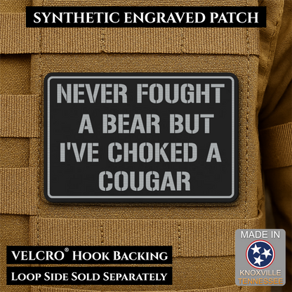 I’ve Choked A Cougar laser-engraved synthetic morale patch: a rectangular black synthetic patch with white engraved text reading “NEVER FOUGHT A BEAR BUT I’VE CHOKED A COUGAR,” shown attached to tan tactical webbing. Text banners.