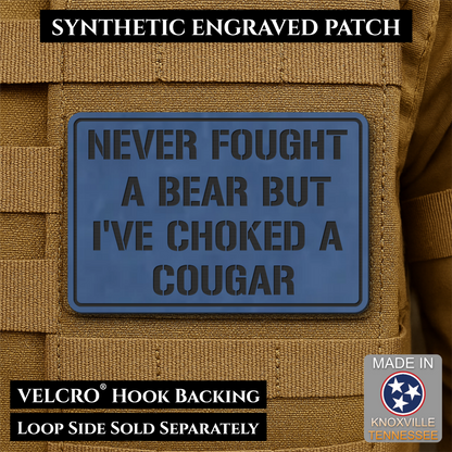 I’ve Choked A Cougar laser-engraved synthetic morale patch: a blue rectangular synthetic engraved patch with black text reading “NEVER FOUGHT A BEAR BUT I’VE CHOKED A COUGAR,” shown attached to tan tactical vest loops. Text banners.