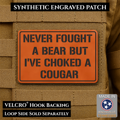 I’ve Choked A Cougar laser-engraved synthetic morale patch: an orange rectangular synthetic engraved patch with black text reading 'NEVER FOUGHT A BEAR BUT I'VE CHOKED A COUGAR' shown attached to tan tactical gear. Black text.