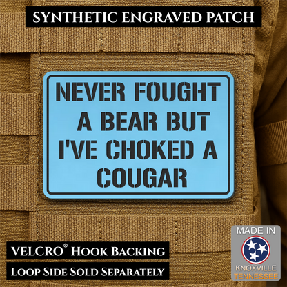 I’ve Choked A Cougar laser-engraved synthetic morale patch: a rectangular synthetic engraved patch with a light blue background and black text reading “NEVER FOUGHT A BEAR BUT I’VE CHOKED A COUGAR,” shown attached to tan tactical.