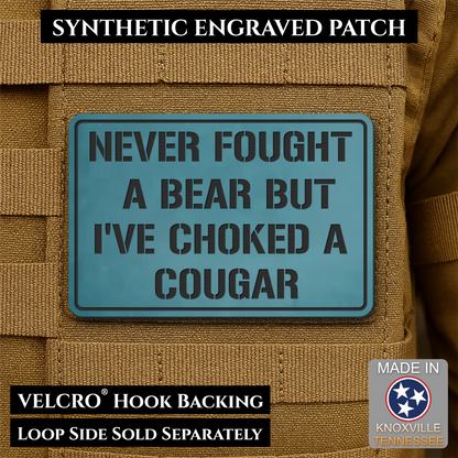 I’ve Choked A Cougar laser-engraved synthetic morale patch: a rectangular synthetic engraved patch with a blue-green background and black text reading 'NEVER FOUGHT A BEAR BUT I'VE CHOKED A COUGAR,' shown attached to tan tactical.