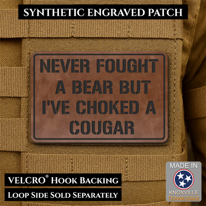 I’ve Choked A Cougar laser-engraved synthetic morale patch: a rectangular synthetic engraved patch with a brown faux-leather look and dark gray text reading 'NEVER FOUGHT A BEAR BUT I'VE CHOKED A COUGAR,' shown attached to tan.