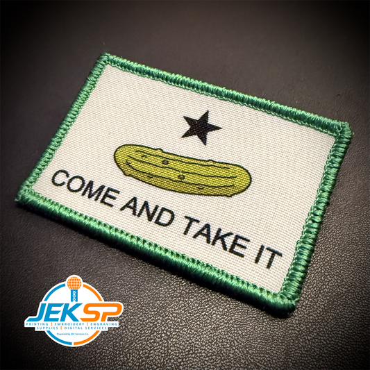 A rectangular embroidered patch with a green border, an off-white center, a black star, a yellow-green pickle illustration, and the text 'COME AND TAKE IT' on a dark textured background. A 'JEKSP' watermark is visible in the lower-left corner.