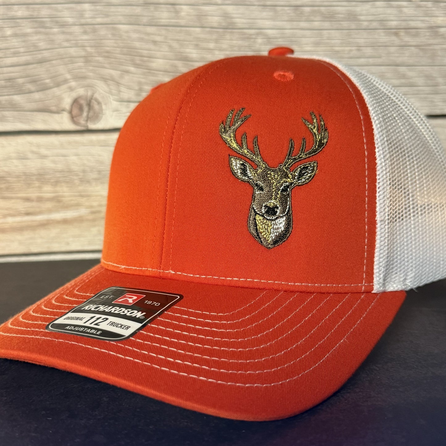 Orange and white cap with deer emblem on a wooden surface