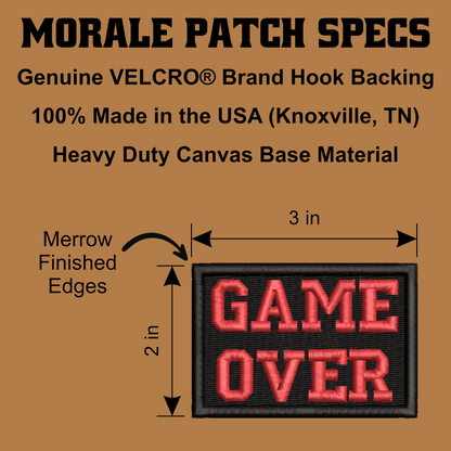 A product specification graphic for a morale patch. The image shows a rectangular black canvas patch with raised red embroidered text reading 'GAME OVER' and includes dimensions labeled 3 in by 2 in, plus text stating 'Genuine VELCRO® Brand Hook Backing,' '100% Made in the USA (Knoxville, TN),' and 'Heavy Duty Canvas Base Material.