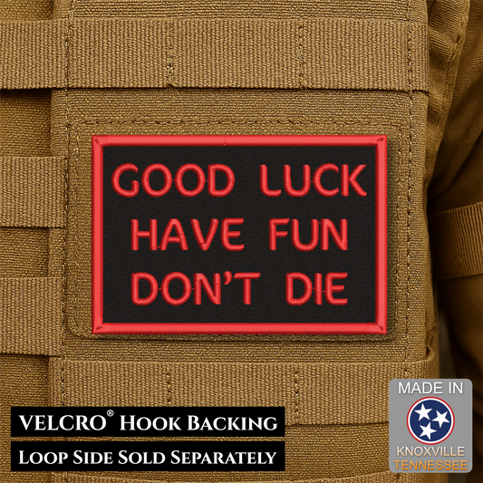 A rectangular black patch with red border and red text reading 'GOOD LUCK HAVE FUN DON'T DIE' attached to tan tactical gear. Text at the bottom says 'VELCRO HOOK BACKING LOOP SIDE SOLD SEPARATELY' and a 'Made in Knoxville Tennessee' badge appears in the lower right.