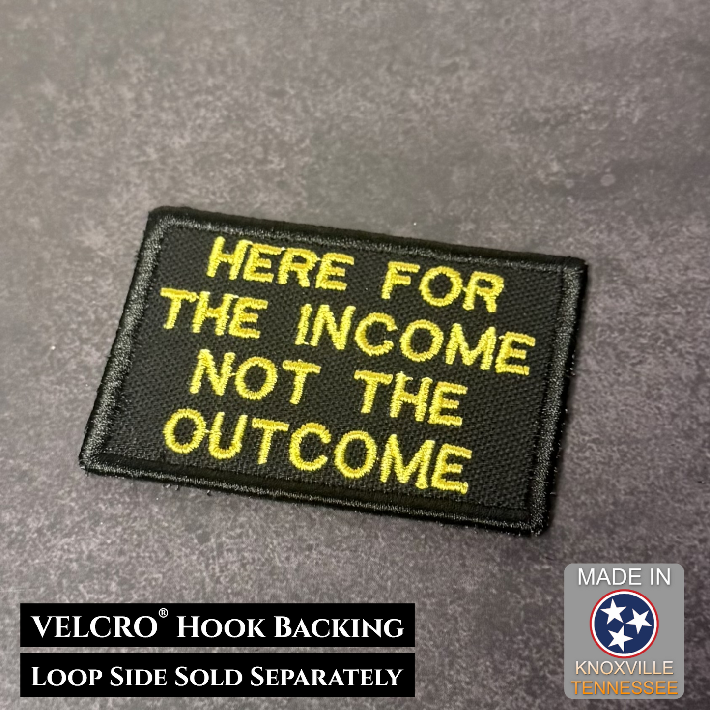 Black patch with yellow text 'HERE FOR THE INCOME NOT THE OUTCOME' on a gray background, with VELCRO hook backing information.