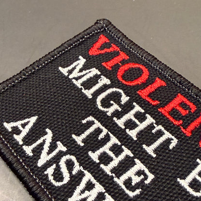 A close-up of a black embroidered patch with white and red text reading 'VIOLENT MIGHT THE ANSWER'.