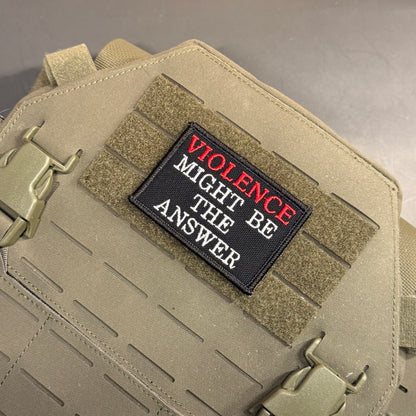 A rectangular embroidered patch with the text 'VIOLENCE MIGHT BE THE ANSWER' in white and red lettering on a black background, attached to tan tactical webbing on a tan bag.