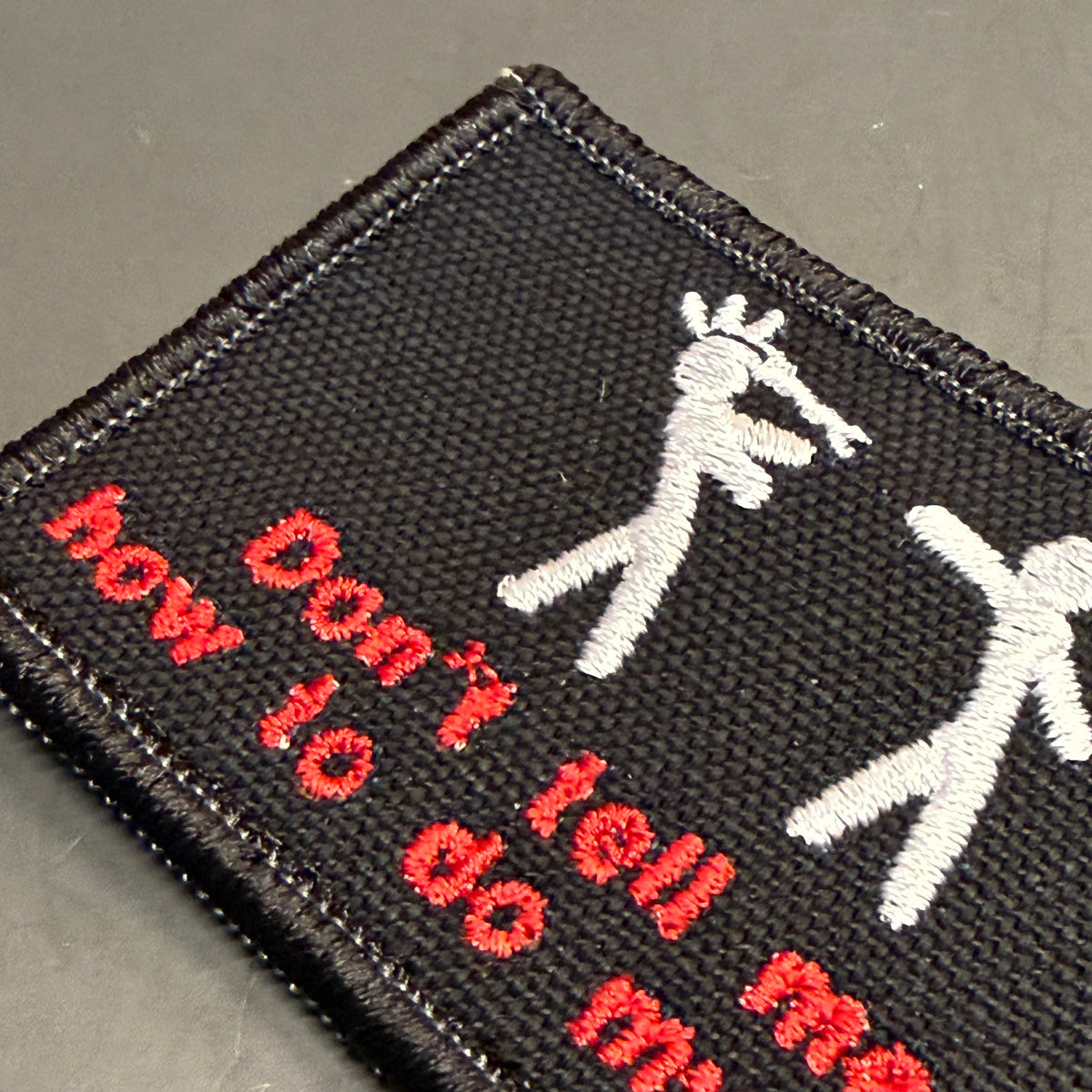 A close-up of a black embroidered patch featuring two white stick-figure style dancers and red text reading 'Don't tell me how to do my.