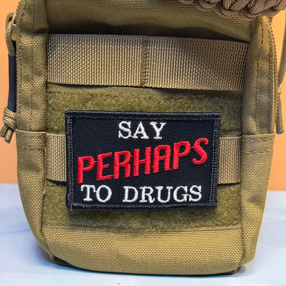 A close-up of a tactical pouch in olive drab webbing with a rectangular embroidered patch that reads 'SAY PERHAPS TO DRUGS' in white and red lettering on a black background.