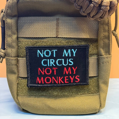 A close-up of a tactical pouch in olive drab nylon with a black embroidered patch that reads 'NOT MY CIRCUS NOT MY MONKEYS' in light blue and red lettering.