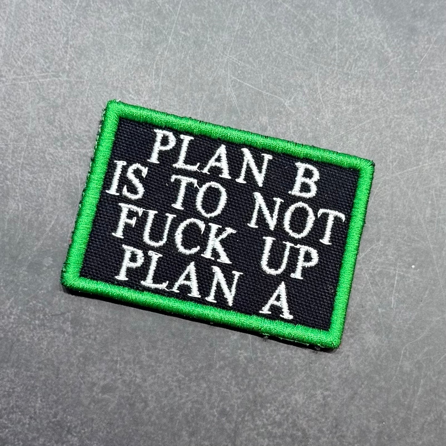 Black embroidered morale patch with a green border and white text reading "Plan B Is To Not Fuck Up Plan A" displayed on a gray background.