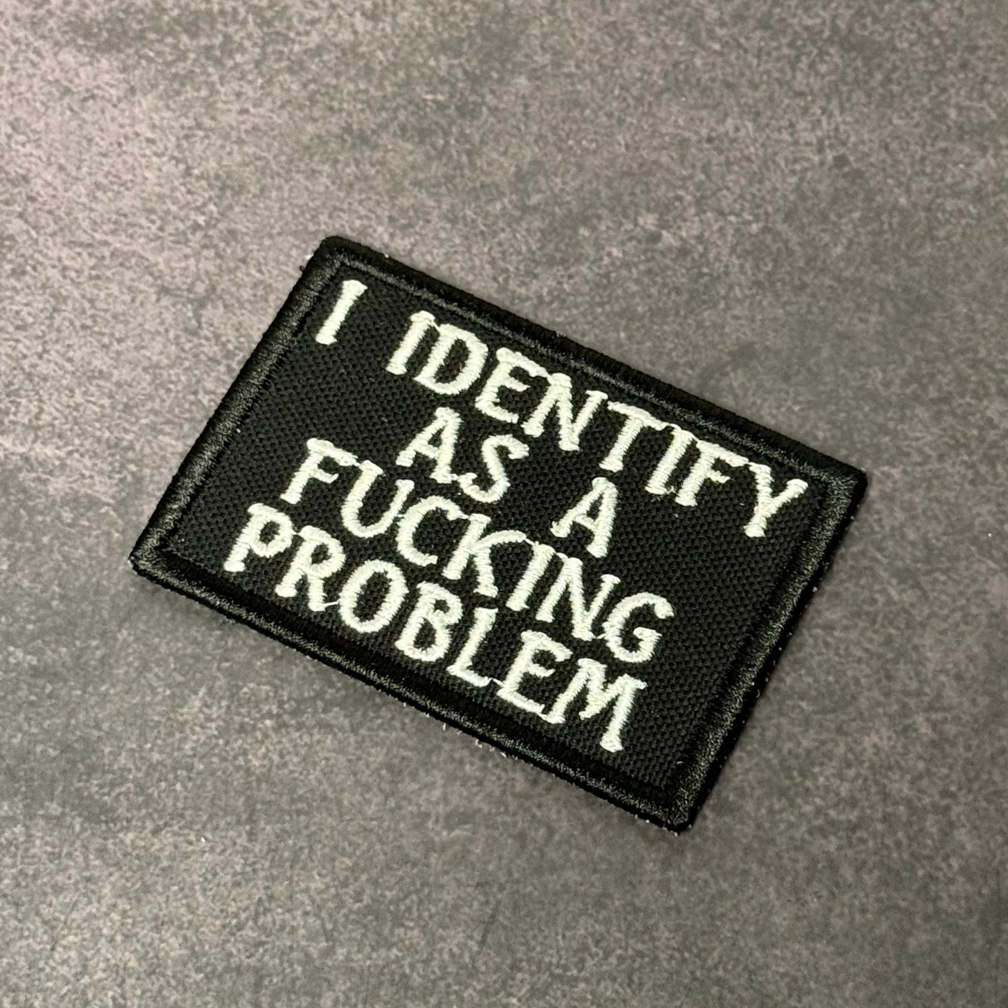 Black embroidered morale patch with white text reading "I Identify As A F-ing Problem" displayed on a gray background.