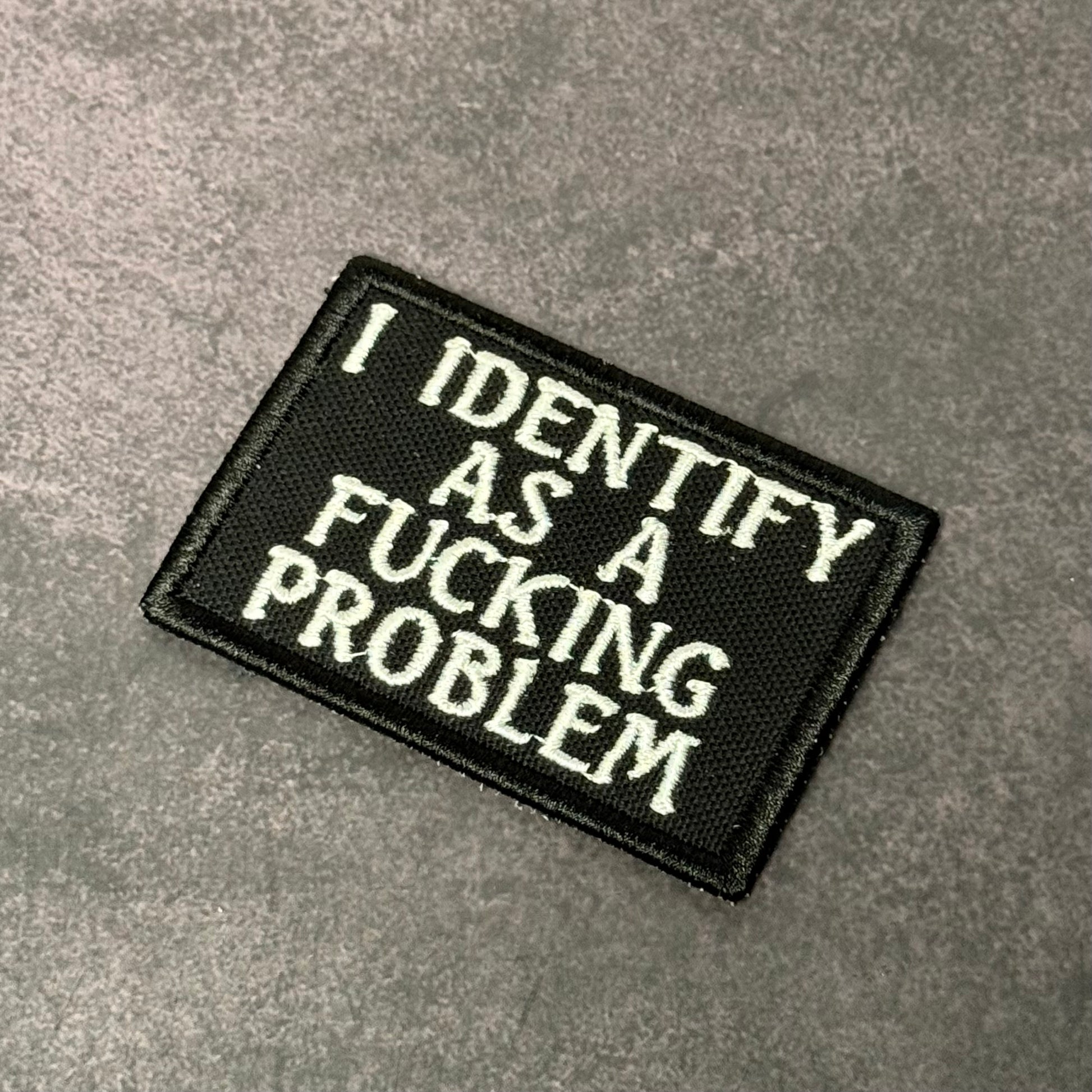 Black embroidered morale patch with white text reading "I Identify As A F-ing Problem" displayed on a gray background.