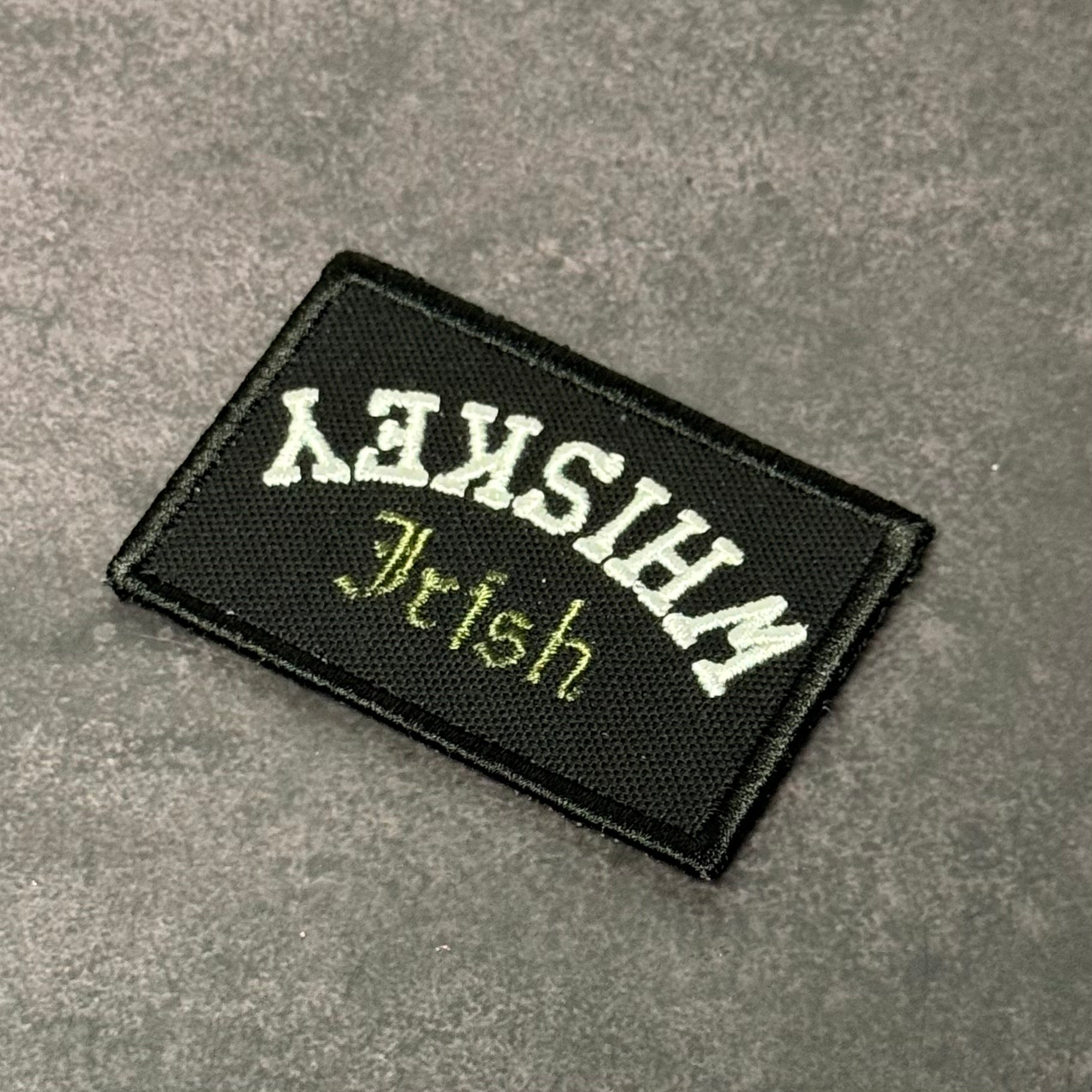 Black embroidered morale patch featuring an upside-down "Irish Whiskey" design in white and green lettering on a gray background.