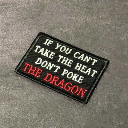 Black embroidered morale patch with white text reading "If You Can't Take the Heat Don't Poke the Dragon" and red accent lettering on a gray background.