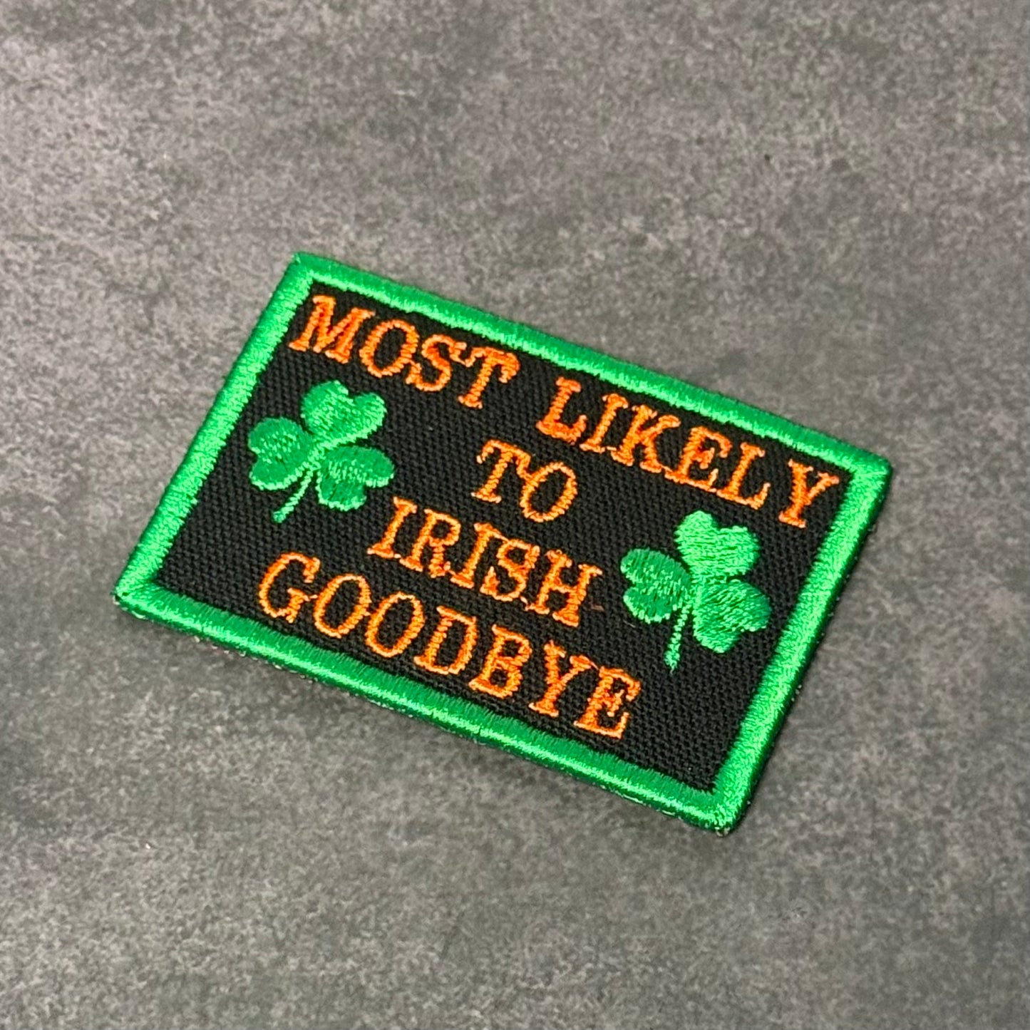 Black embroidered morale patch with green border, green shamrocks, and orange text reading "Most Likely To Irish Goodbye" displayed on a gray background.