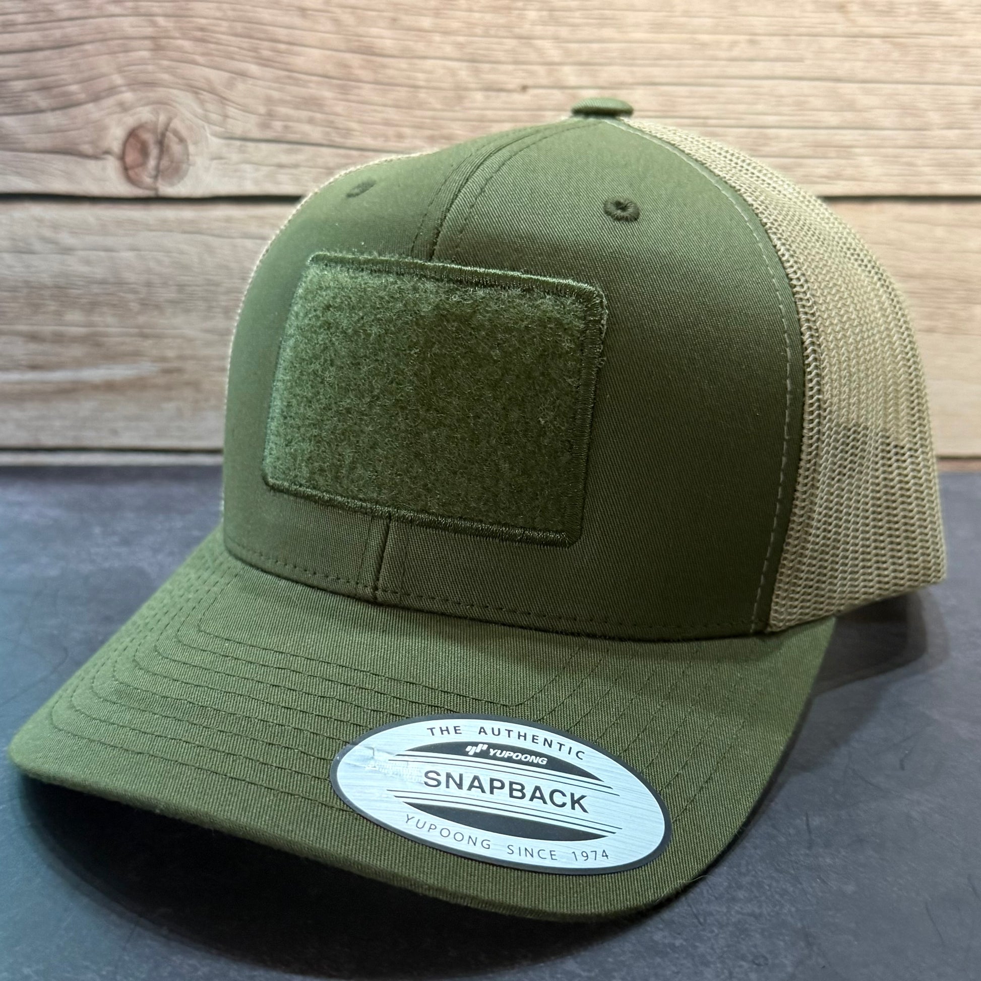 Green snapback cap with a velcro patch on a panel on the front.