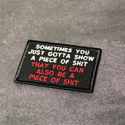 Black embroidered morale patch with white and red text reading "Sometimes You Just Gotta Show a Piece of Shit That You Can Also Be a Piece of Shit" displayed on a gray background.