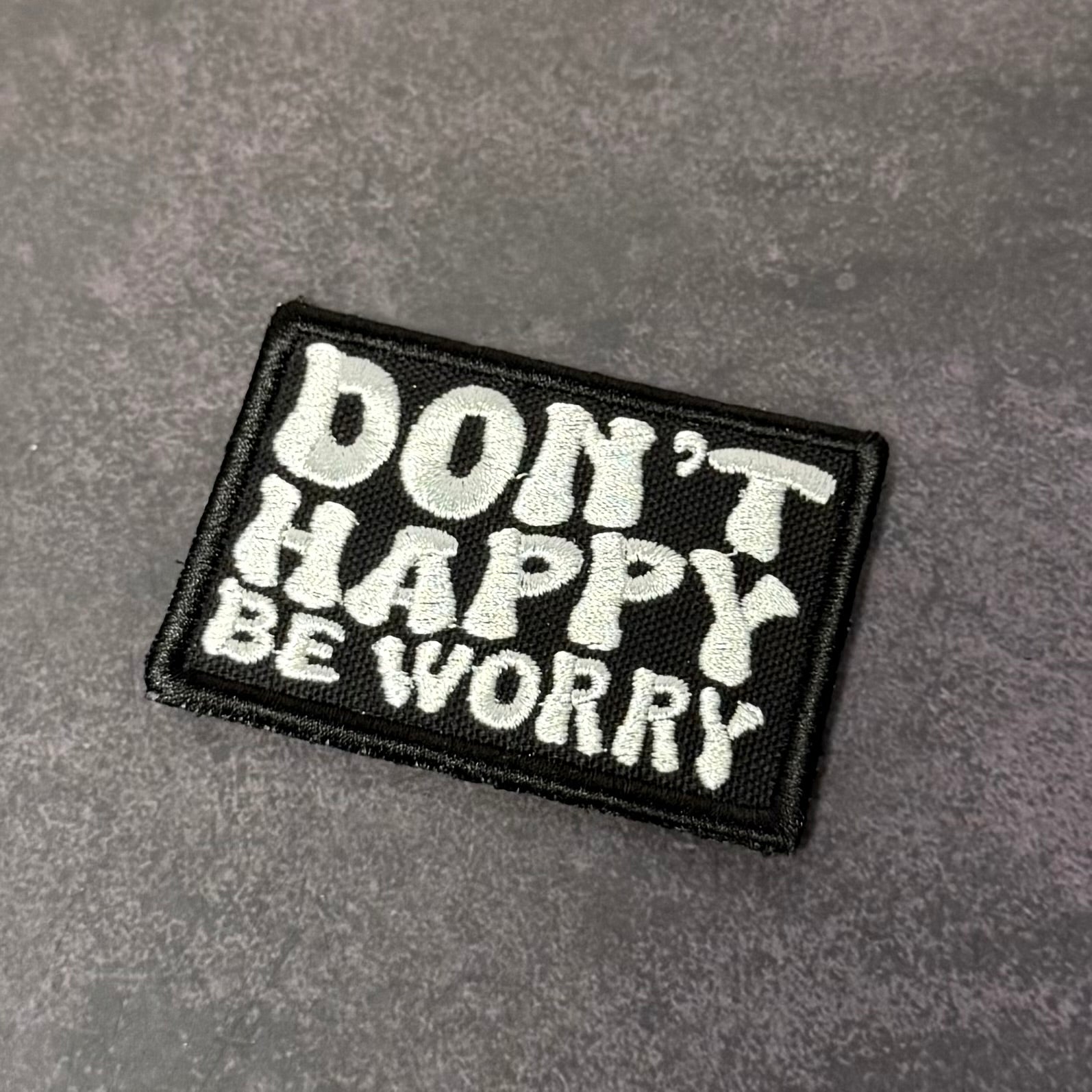Black embroidered morale patch featuring the phrase "Don't Happy, Be Worry" in bold white lettering on a gray background.