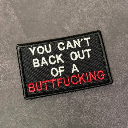 Black embroidered morale patch with white and red text reading "You Can't Back Out Of A Buttfucking" displayed on a gray background.