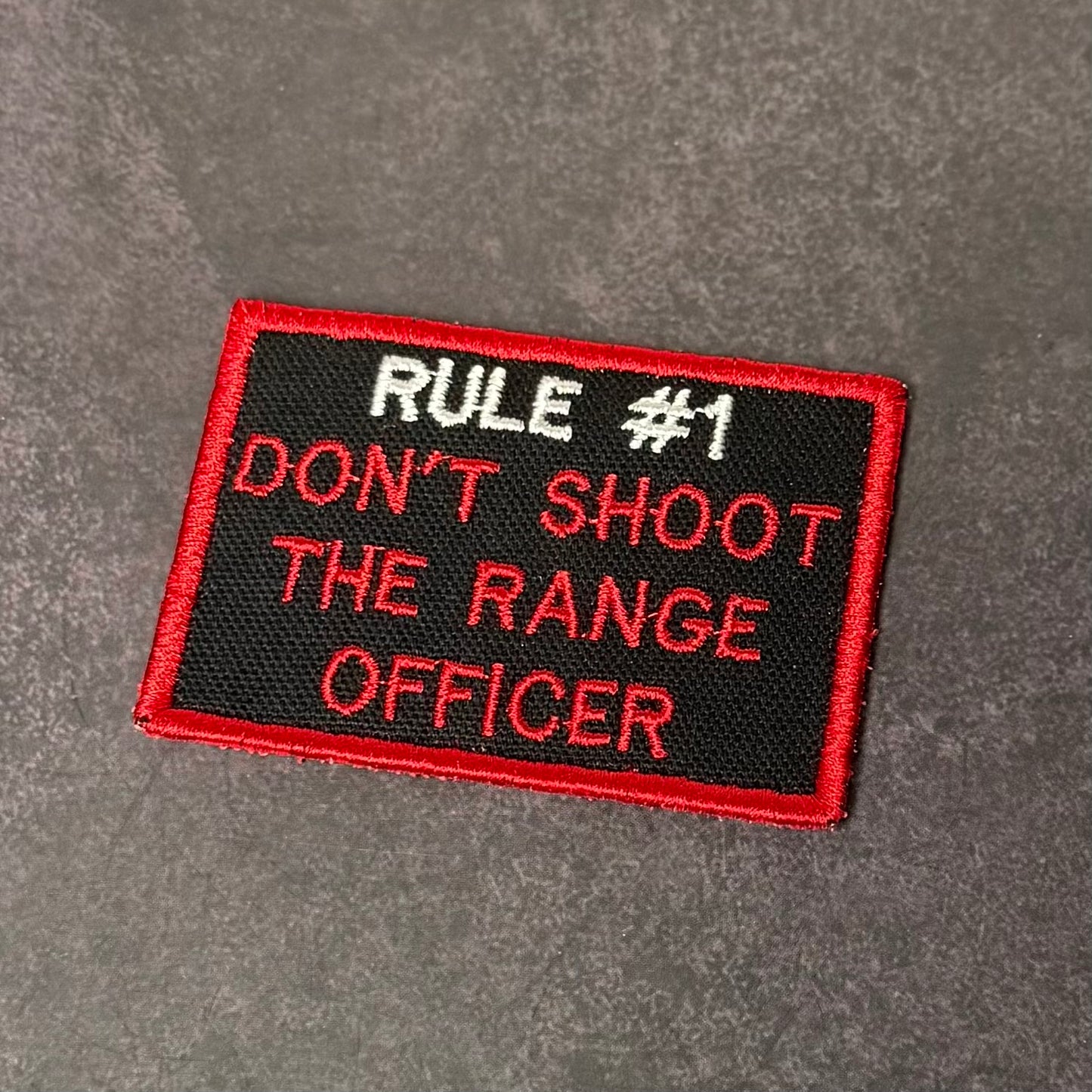 Black embroidered morale patch with red border featuring the humorous phrase "Rule #1 Don't Shoot The Range Officer" in red and white lettering.