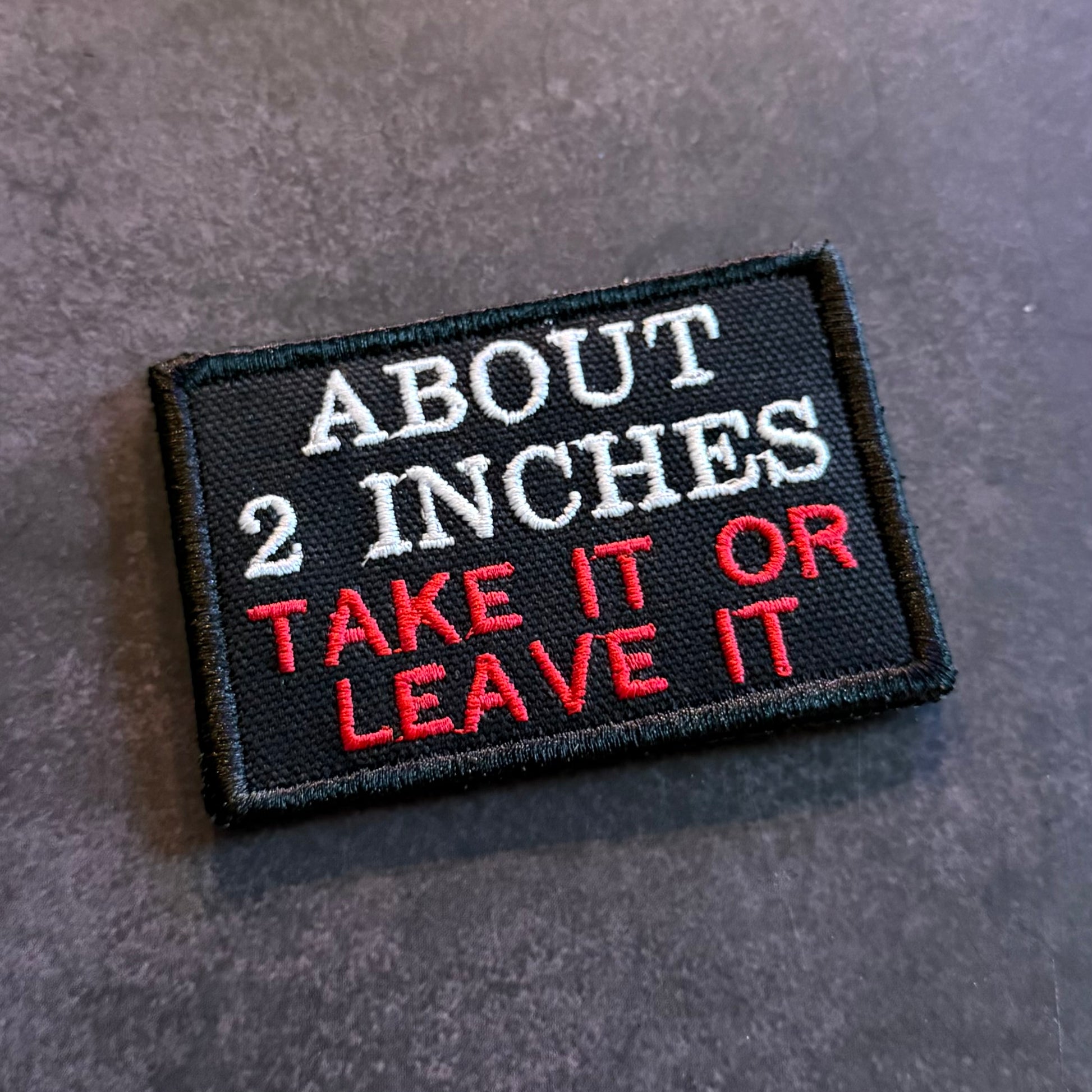 Black embroidered About 2 Inches Take It or Leave It funny morale patch with white and red lettering