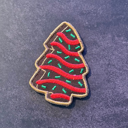 An embroidered Christmas tree patch with red wavy stripes, green pine needles, and a tan stitched border on a dark textured background.